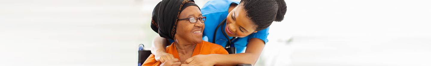 An elderly black woman and a female nurse smiling at each other